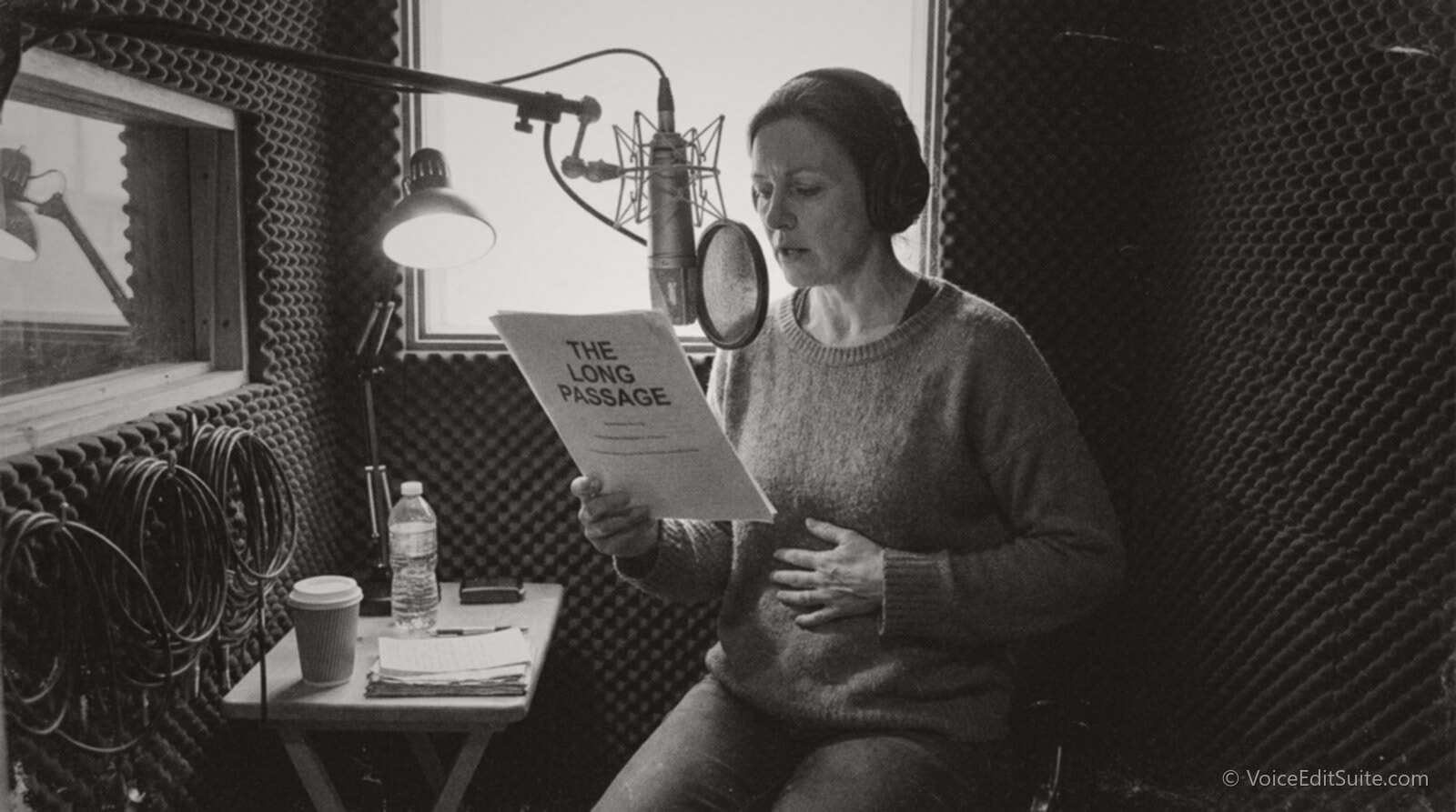Black and white photograph of a narrator at the microphone taking a deep breath, hand on her stomach