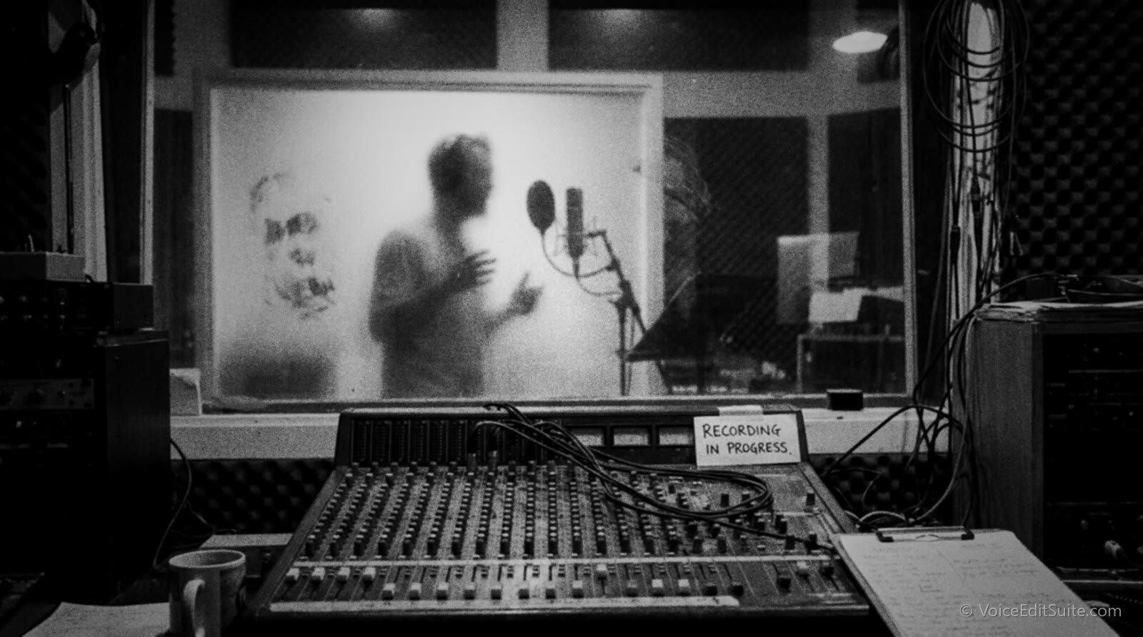Black and white photograph of an anonymous figure behind frosted glass in a recording booth, only a silhouette visible