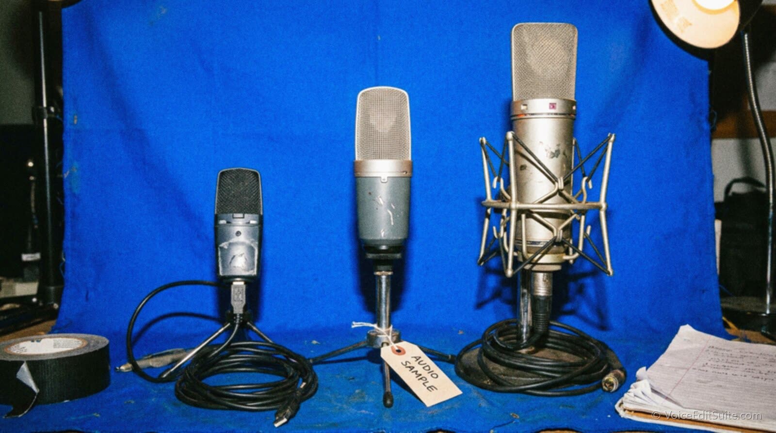 Three microphones of rising price lined up on a bright blue backdrop, from a cheap USB mic to a studio condenser