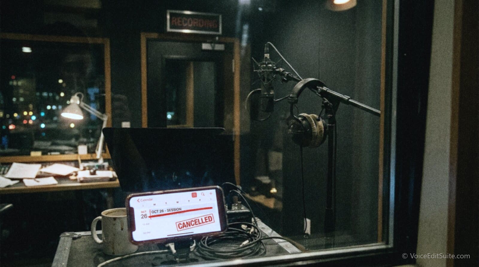 An empty recording booth at night with the session light switched off and a phone showing a cancelled calendar event