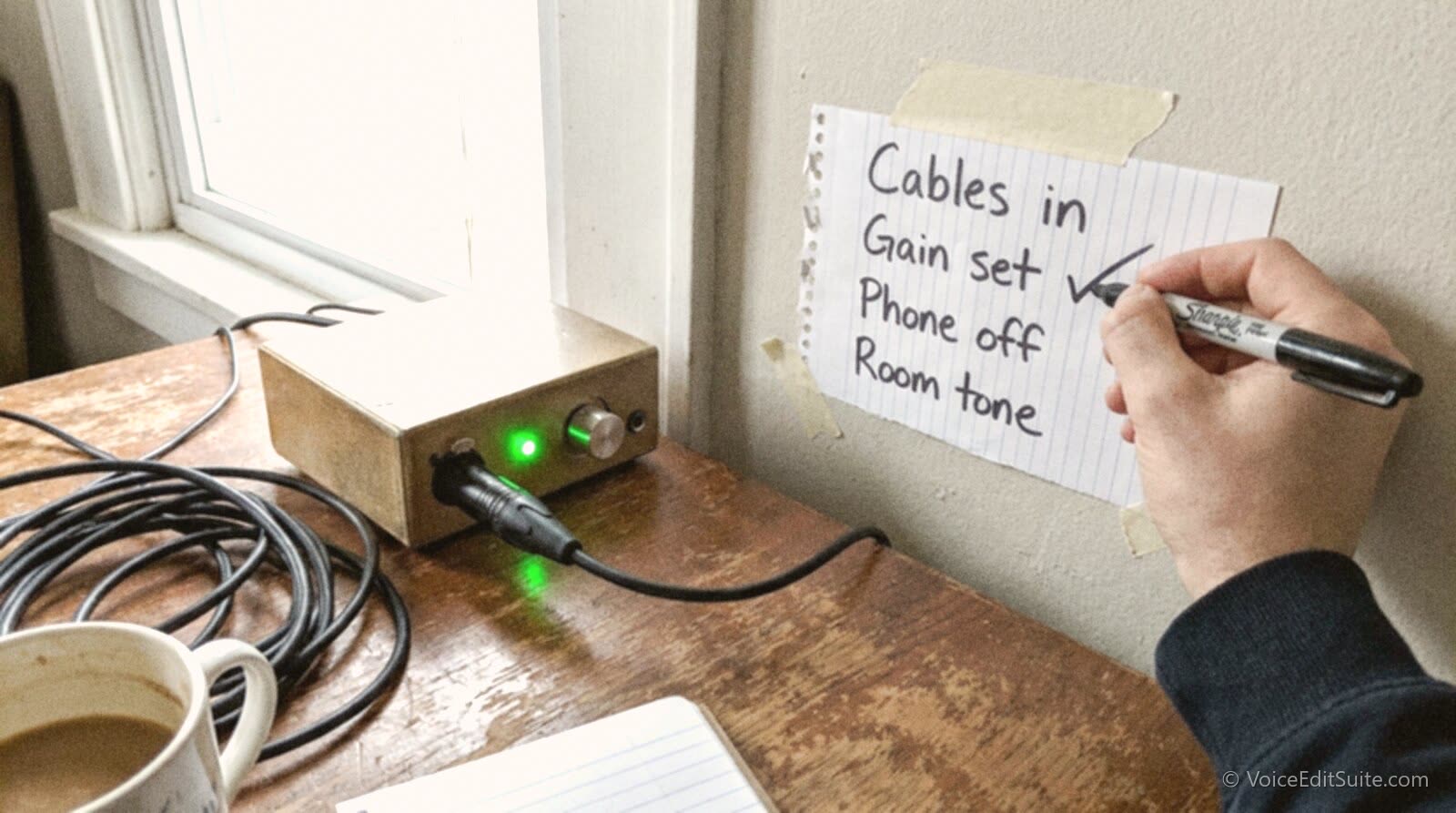 A voice actor's hand checking off a pre-session checklist taped beside the audio interface