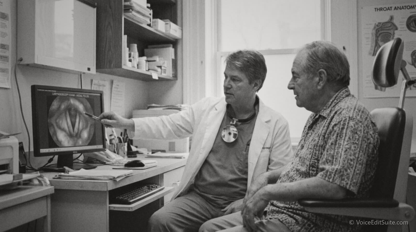 Black and white photograph of a laryngologist showing a patient an image of vocal folds on a screen