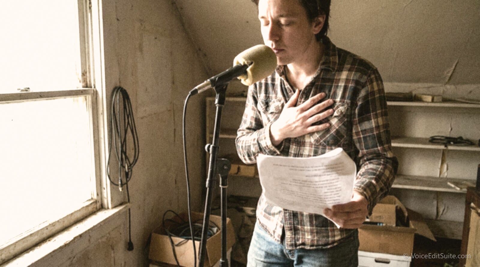 A narrator at a home microphone stand with one hand flat on their chest, feeling for chest resonance while reading a line