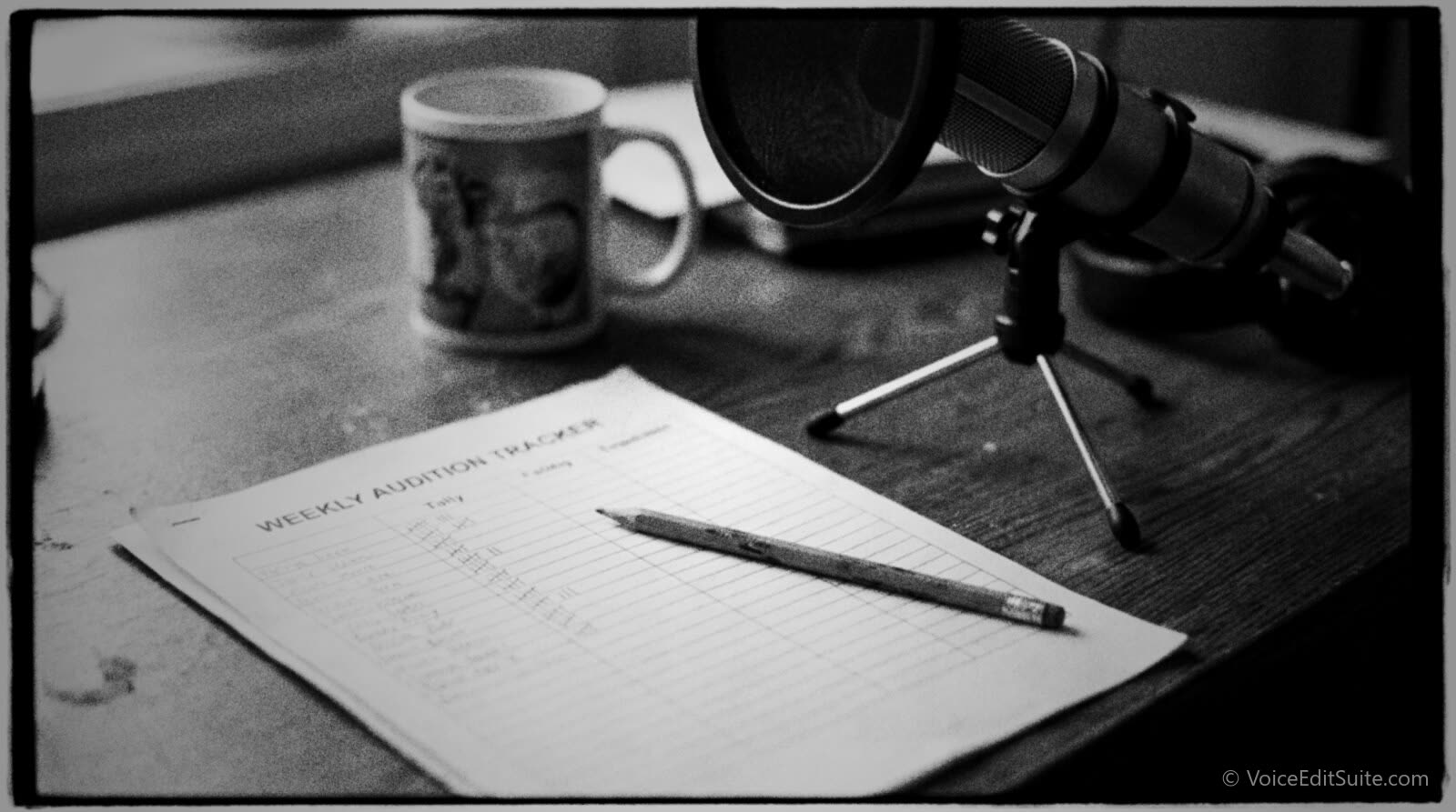 A voice actor's desk with a printed weekly audition tracker covered in handwritten rows and tally marks, a pencil and a microphone on a desk stand beside it